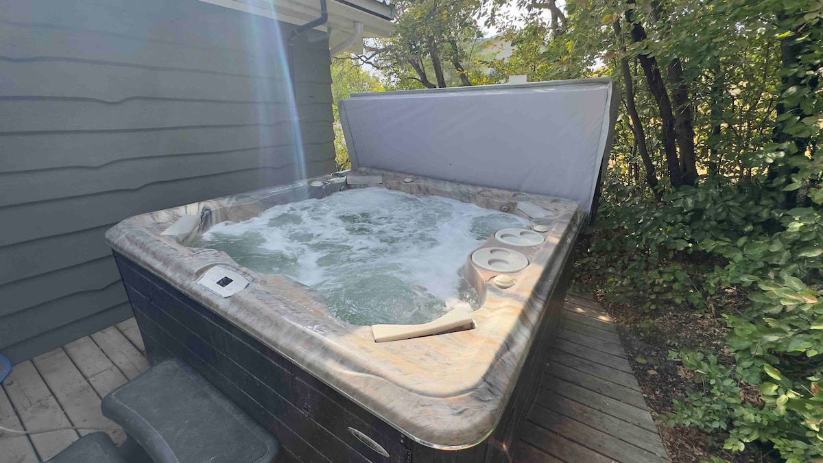A hot tub surrounded by lush greenery provides a relaxing outdoor space. Its bubbling water invites guests to unwind, while the wooden deck layout emphasizes a private and tranquil atmosphere. A cover rests partially opened, hinting at easy access for guests.