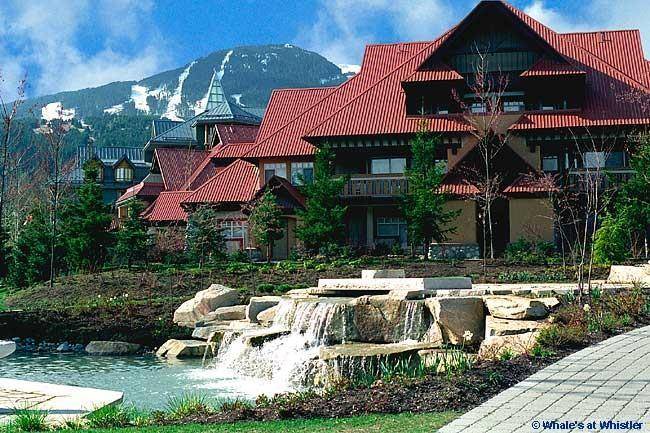The exterior of the Sunpath complex showcases a multi-level structure with a distinctive red roof. Surrounding greenery complements a serene water feature flowing over rocks, with mountains visible in the background. The scene captures the charm of the area and its natural beauty.