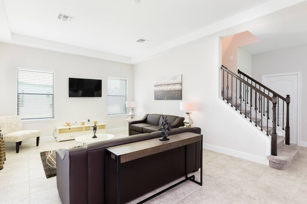 The living area is bright and modern, featuring comfy sofas and a TV.