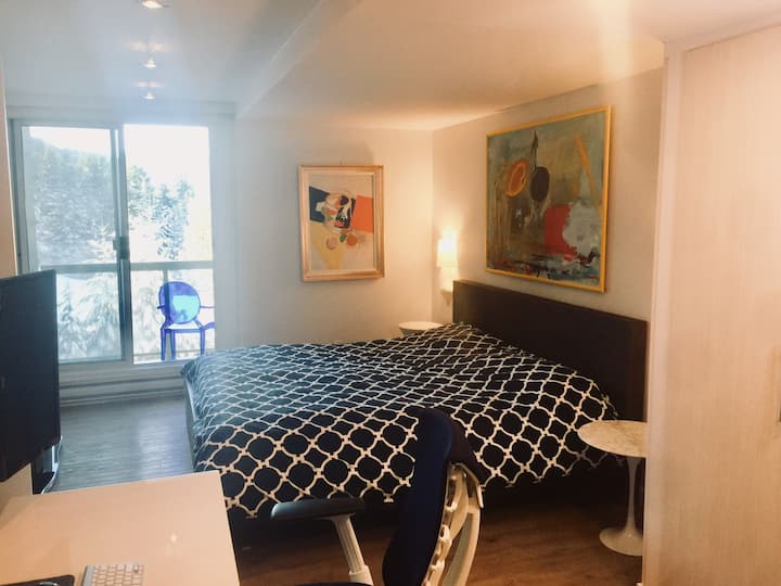 Chambre principale avec lit king size et écran TV incurvé ; petit balcon avec coin salon juste à l'extérieur, face aux pistes de ski.