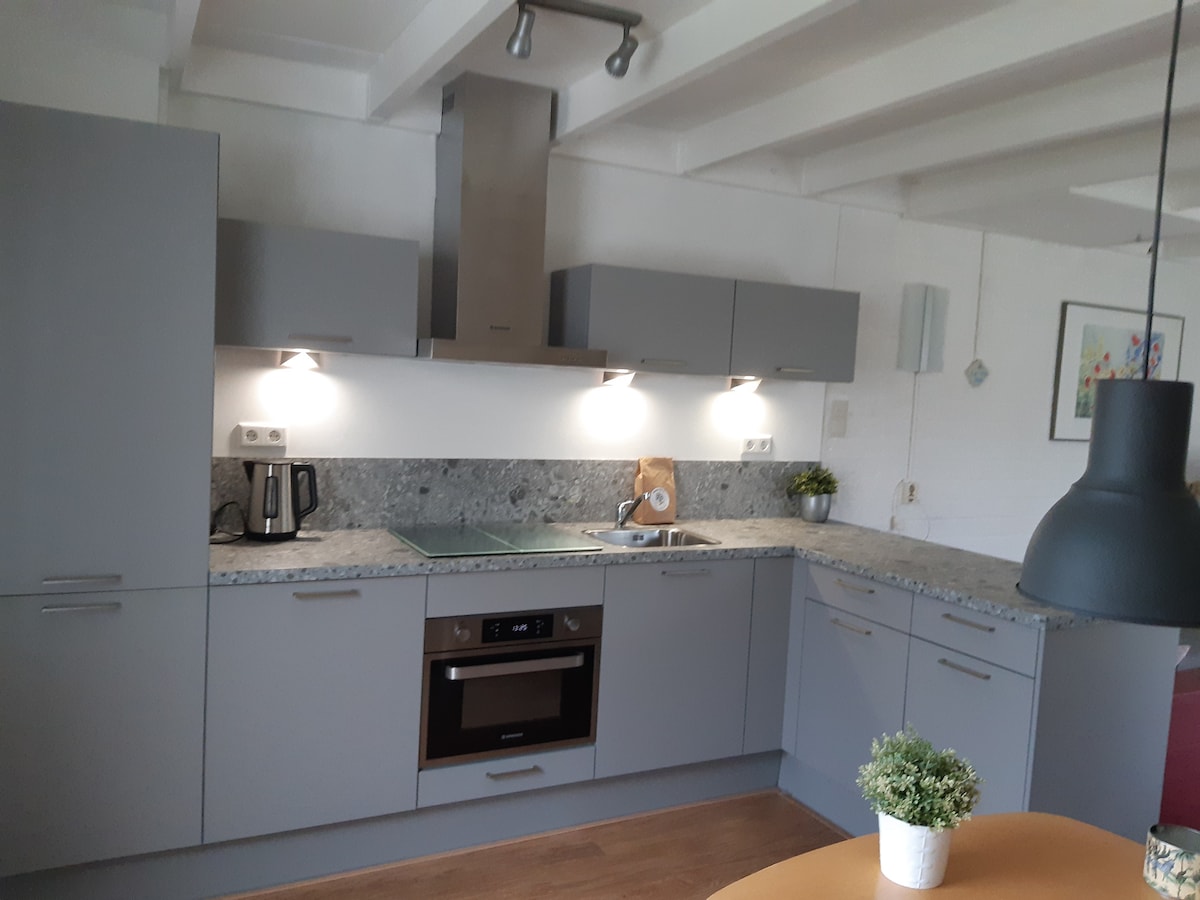 A modern kitchen features gray cabinetry and a speckled countertop. Stainless steel appliances include an oven and a coffee maker. Soft lighting is provided by mounted fixtures above the workspace, creating a functional cooking area. A small potted plant is placed on the countertop for a touch of greenery.