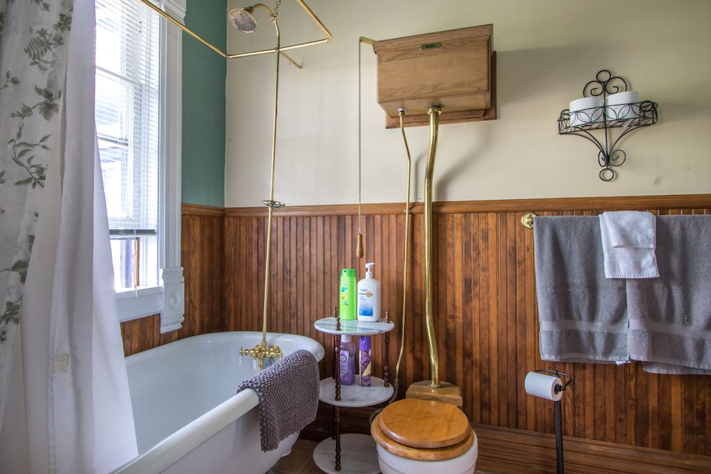 Private en-suite bathroom with shower over claw-foot tub and high tank toilet.