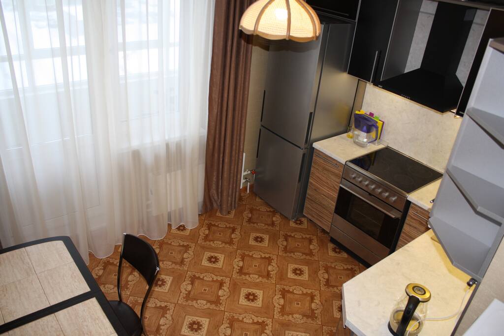 A kitchen equiped with a dinner table, a fridge, a cooker and an oven, a microwave oven, and a kettle