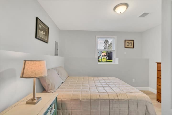 غرفة نوم في الطابق السفلي مع سرير كامل الحجم ومكتب وطاولة بجانب السرير وخزانة كبيرة