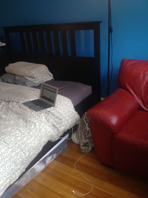 Queen size bed with leather chair for work space in room.
