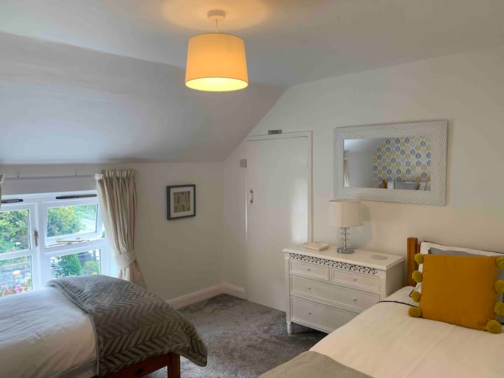 Dhoma e dytë e gjumit që tregon disa nga karakteristikat e vilës me tavane të pjerrëta dhe dritare të ulëta me pamje nga kopshti i përparmë. Kjo dhomë gjumi përmban dy krevate tekë për të rritur dhe të çon drejtpërdrejt në banjën e familjes.