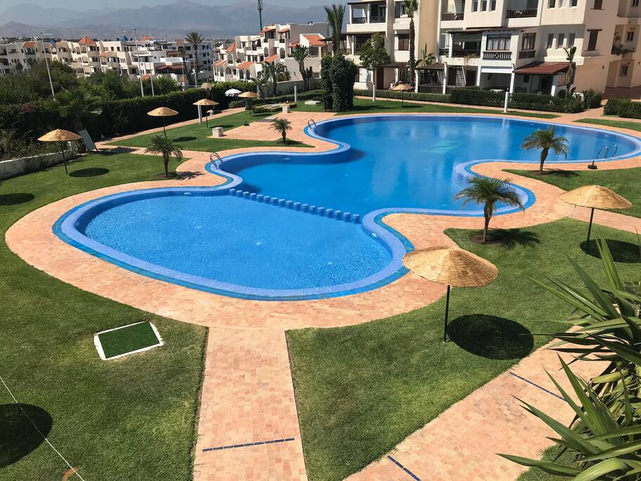 Les piscines du complexe bordés par une belle verdure avec des parasols