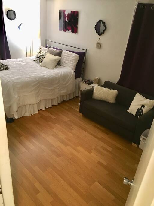 Spacious bedroom featuring a queen sized bed, hardwood floors, love seat and double closets