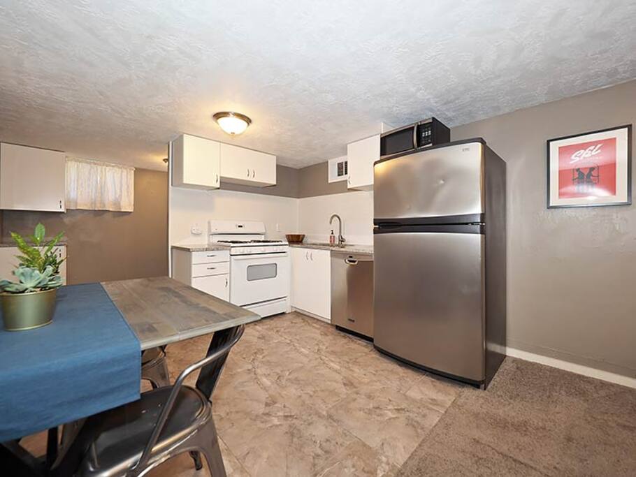 View of dining table and fully stocked kitchen complete with microwave, toaster, dishes, coffee grinder and french press.
