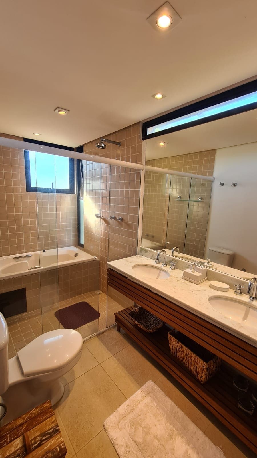 A well-appointed bathroom features a glass-enclosed shower and a separate bathtub. Dual sinks are positioned on a wooden vanity beneath a mirror. Natural light enters through a nearby window, and neutral tiles create a cohesive atmosphere in the space.