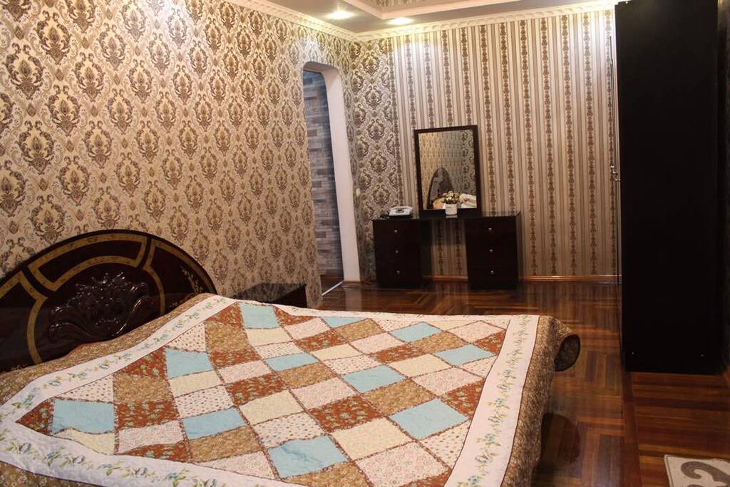 Bedroom with king size bed, wardrobe, mirror table, two (bed) side drawers and small table in the corner