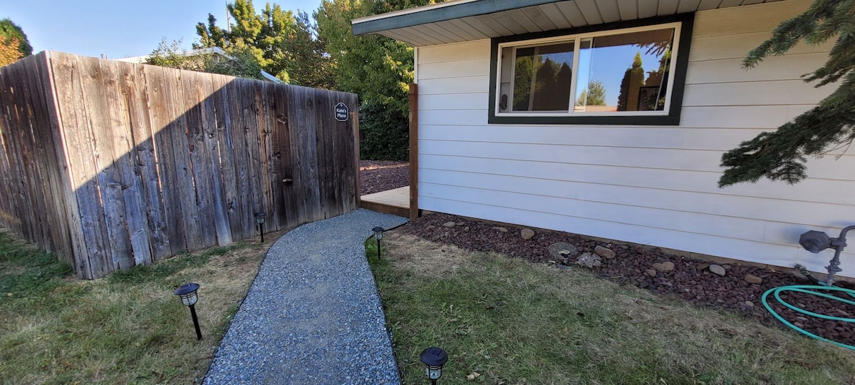 A well-maintained pathway leads to the entrance of the private dwelling, framed by a wooden fence. Soft garden lights are positioned along the gravel path, and a patch of grass is visible on either side, contributing to a welcoming outdoor area.