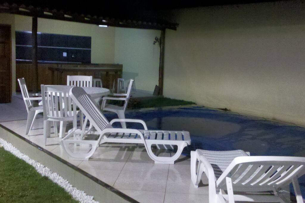 Área externa. Piscina, churrasqueira, pia, mesa e banheiro.