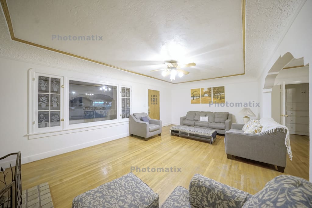 It is a living room with large and beautiful windows. You can see grass and palm trees in the front yard. Of course, curtains are also installed.