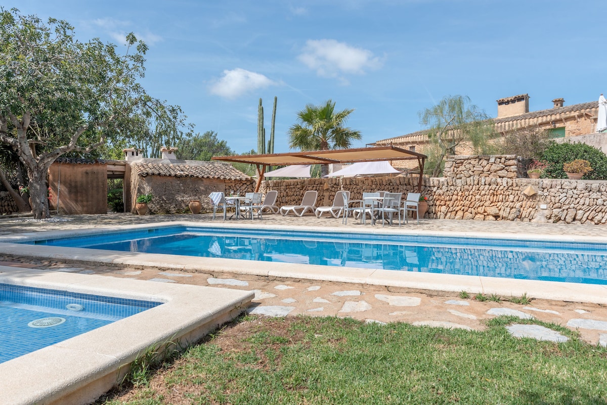 A shared outdoor pool area is featured, with a larger swimming pool alongside a smaller children's pool. Sun loungers line the poolside, inviting relaxation. Lush greenery surrounds the space, complemented by a shaded seating area that offers comfort and respite from the sun.