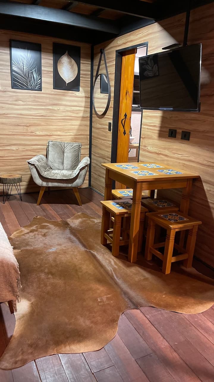 Perspectiva da sala decorada com tapetes temáticos, tv e futon casal que pode ser aberto para ver tv