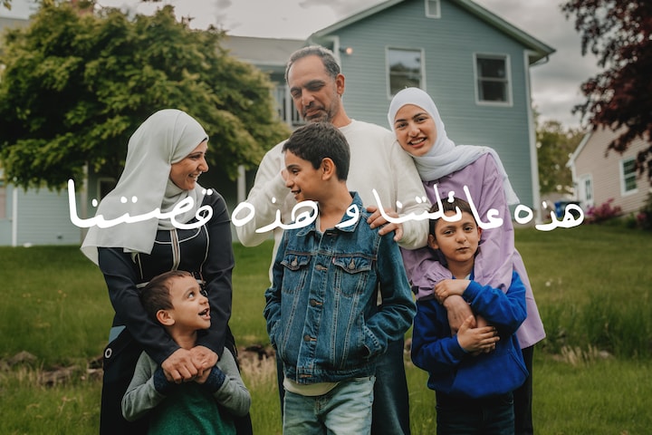 Eine sechsköpfige Familie syrischer Geflüchteter steht lächelnd zusammen im Hinterhof eines blauen Hauses.