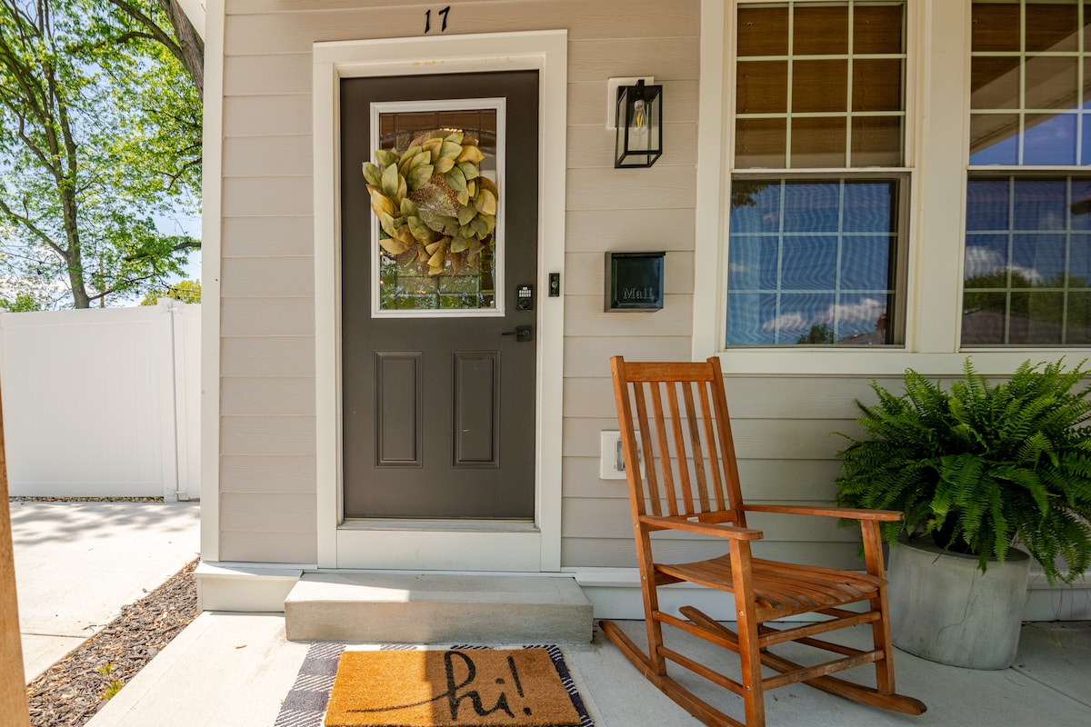 The entrance features a welcoming front door adorned with a seasonal wreath. A wooden rocking chair is placed on the porch next to a potted plant. The doormat displays a friendly greeting, enhancing the inviting appearance of the home.