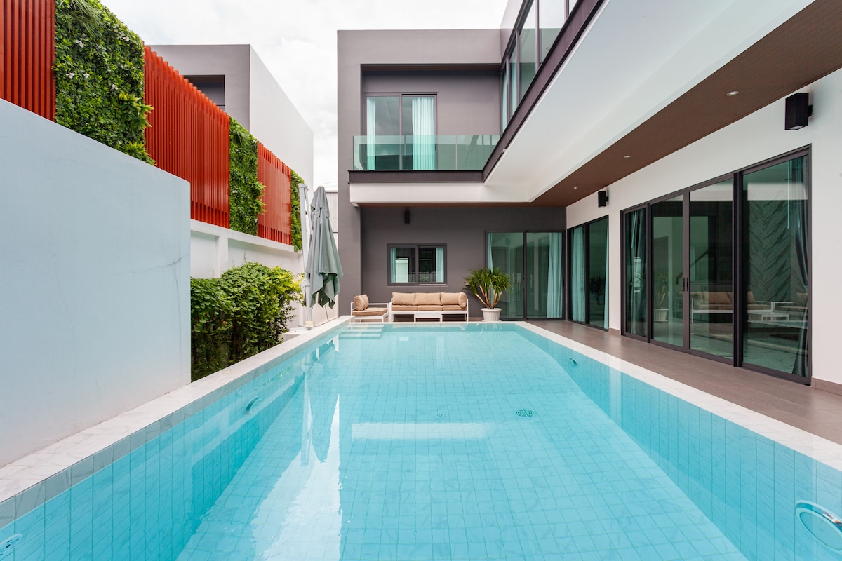 A private swimming pool is featured within the villa, surrounded by a well-maintained area. The space includes lounging chairs and greenery, contributing to a serene atmosphere. Large glass doors offer views of the indoor areas, enhancing the connection between the outdoor and indoor spaces.