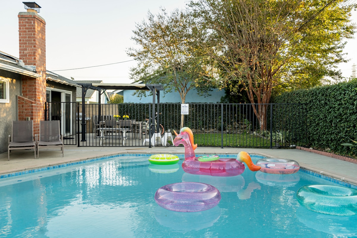 A private swimming pool is surrounded by a safety fence, featuring colorful floats in various shapes. Comfortable lounge chairs are positioned nearby, and a covered terrace can be seen in the background, providing ample space for outdoor gatherings.