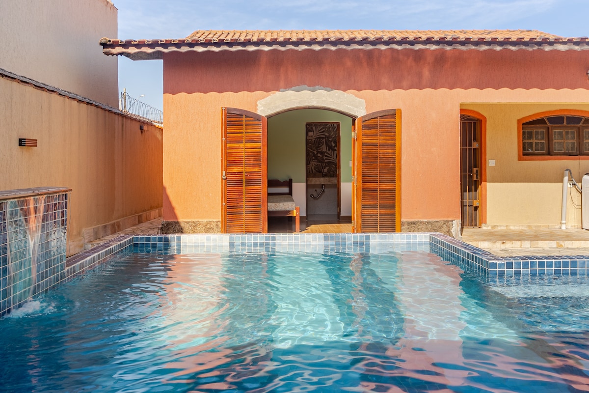 An inviting outdoor space features a shimmering pool, surrounded by a tiled deck. Large wooden doors open to reveal the interior, allowing for an airy connection between the pool area and living spaces.
