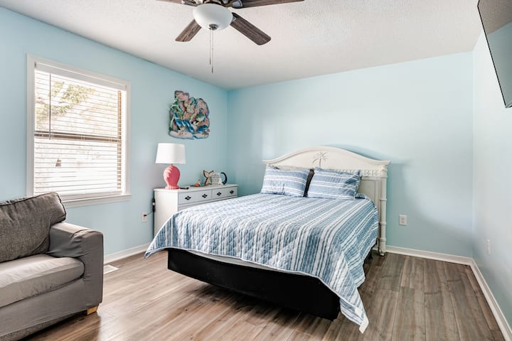 [Huvudnivå] Detta ljusa sovrum vid kusten erbjuder en bekväm queensize-säng med randiga sängkläder, en mysig soffa och gott om naturligt ljus. En byrå, öppen garderob och väggmonterad TV gör det enkelt att slå sig till ro perfekt för avkoppling efter en dag på stranden.