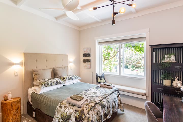 Bright and cozy bedroom with a tufted headboard, floral bedding, a bench by the window, and soft lighting, creating a serene atmosphere.