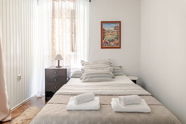 Спалня номер едно с различен комплект чаршафи на леглото. През прозореца можете да виждате през завесите, така че светлината може да влиза през деня. 
През нощта има дървени щори, които да ви предпазят от сутрешната светлина 