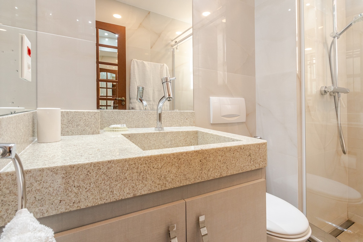 The bathroom features a modern design with a light marble countertop and a sleek sink. A large mirror reflects the space, while a walk-in shower with a glass door is present. Soft towels are neatly arranged, contributing to a tidy atmosphere.