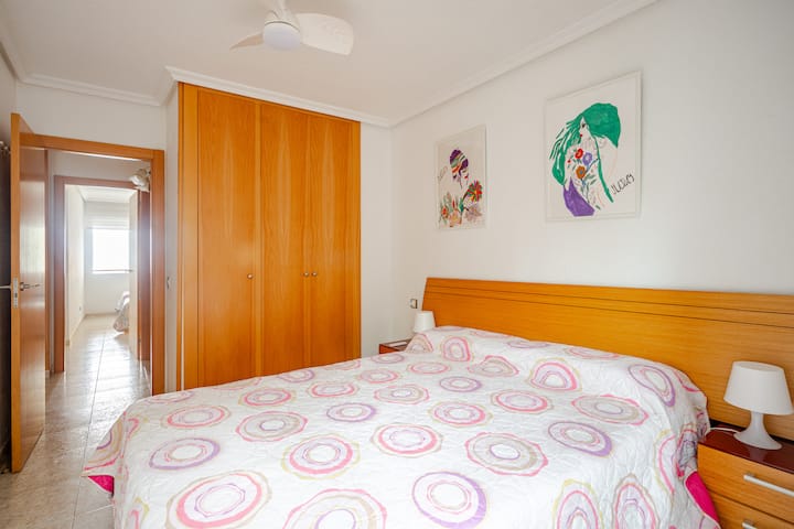 Luminoso dormitorio doble con una cómoda cama, amplio armario empotrado, ventilador de techo y coloridas obras de arte. Hay una cuna disponible bajo petición.