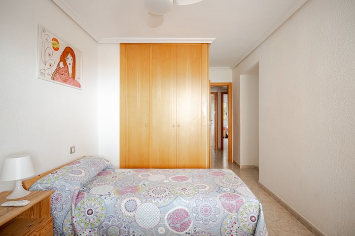 Luminoso dormitorio doble con una cama cómoda, un amplio armario empotrado, mesita de noche y coloridas obras de arte.