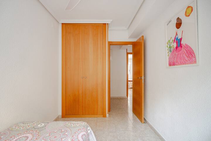 Habitación con armario empotrado, ventilador de techo y obras de arte coloridas, que ofrece un práctico espacio de almacenamiento y un ambiente luminoso y acogedor.