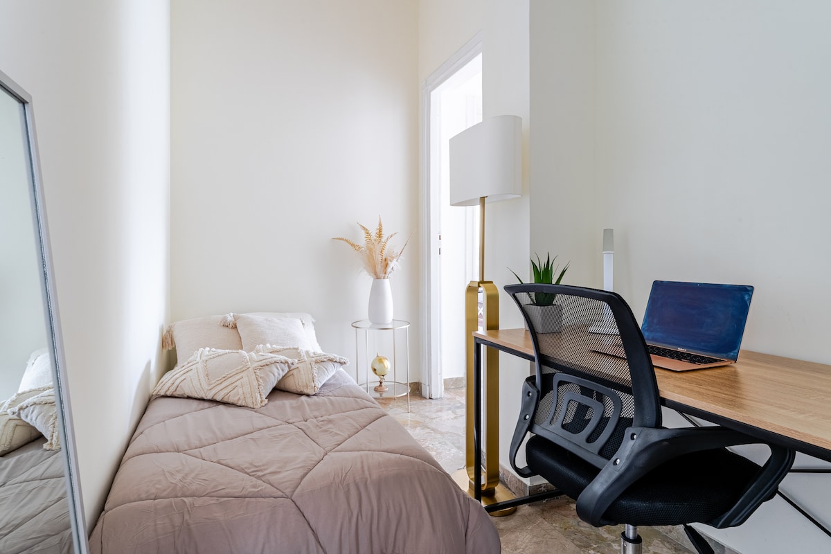 Dhomë e vogël e lezetshme ngjitur me dhomën e ndenjjes që përbëhet nga një krevat tek dhe një qoshe studimi.