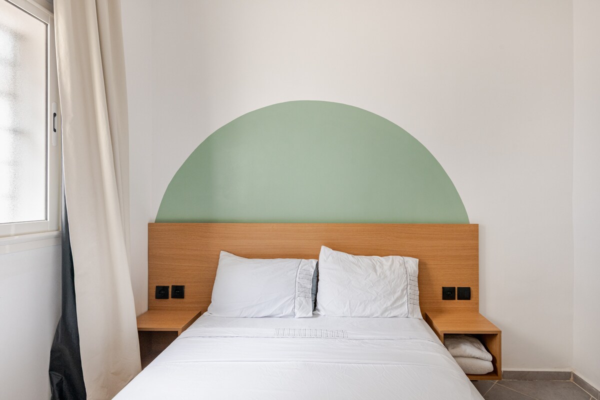 mirna soba čistog dizajna. Odlikuje se umirujućim zelenim zidnim lukom. Bračni krevet s besprijekornom bijelom posteljinom i svijetlim drvenim uzglavljem s visećim noćnim ormarićima. Zen i prirodna atmosfera 