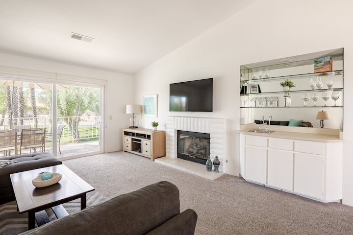 Priestranná obývačka, ktorá dostáva dostatok prirodzeného svetla. Zahŕňa inteligentný televízor, plynový krb a bar v retro štýle.