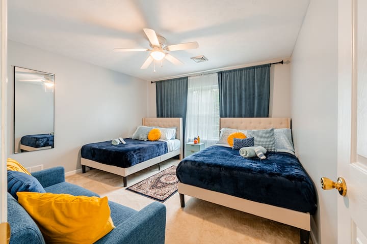 Habitación luminosa y espaciosa con dos lujosas camas tamaño queen, un acogedor sofá y una decoración moderna. Las grandes ventanas aportan luz natural, mientras que la suave ropa de cama azul marino y los alegres detalles crean un espacio cálido y acogedor, perfecto para que las familias o los grupos se relajen con comodidad.