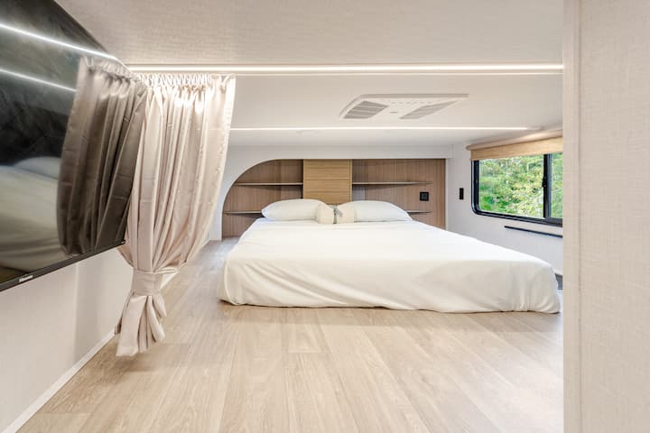 Spacious loft bedroom with a cozy bed, built-in desk for remote work, flat-screen TV, and natural light. Perfect for relaxing, streaming, or working comfortably during your stay