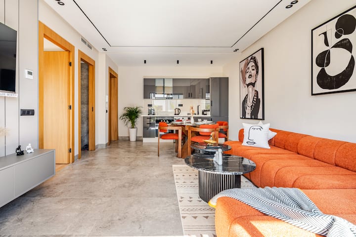 พื้นที่นั่งเล่นแบบเปิดโล่งกว้างขวางพร้อมโซฟาเทอร์ราโคตต้า โต๊ะรับประทานอาหารสำหรับ 4 คน พรมลายกราฟิก และโต๊ะกาแฟทรงประติมากรรม ทีวีติดผนังพร้อมเน็ตฟลิกซ์และช่องนานาชาติ ไฟเบอร์ความเร็วสูง พื้นที่สว่างและสะดวกสบายสำหรับการพักผ่อนและทำงานทางไกล