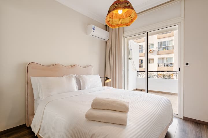 Habitación luminosa con cama doble, cabecero beige, aire acondicionado y acceso al balcón. »