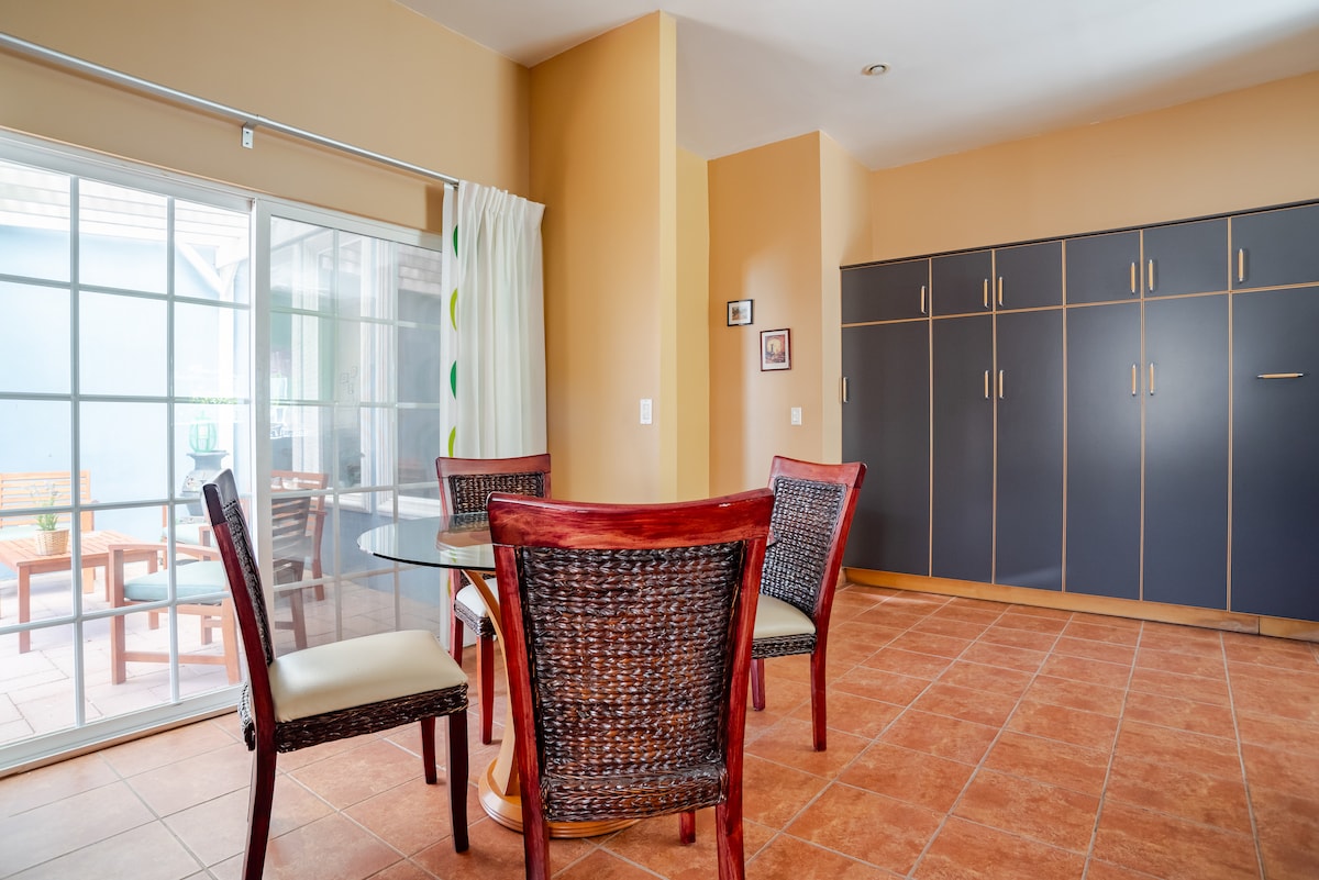 The dining area features a round glass table surrounded by four woven chairs. A large sliding glass door opens to the patio, allowing natural light to brighten the space. A built-in cabinet occupies one wall, providing additional storage.