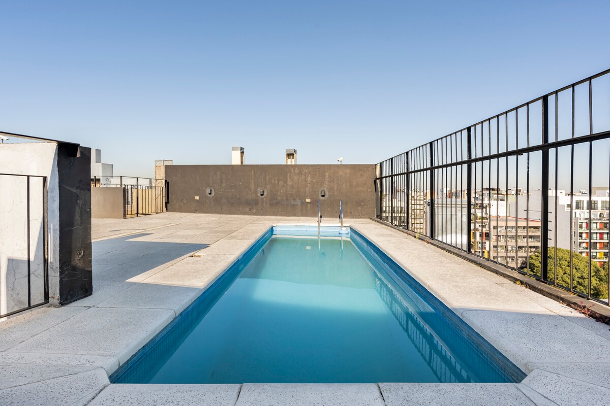 A rooftop pool is viewable, surrounded by a spacious terrace that offers open city views. The water is clear and inviting, while the surrounding area is characterized by sleek railing and minimalistic design elements, providing a modern atmosphere for relaxation.