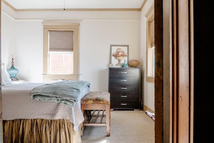 The primary bedroom is off the kitchen with a king bed, chest of drawers, nightstands, and a luggage rack