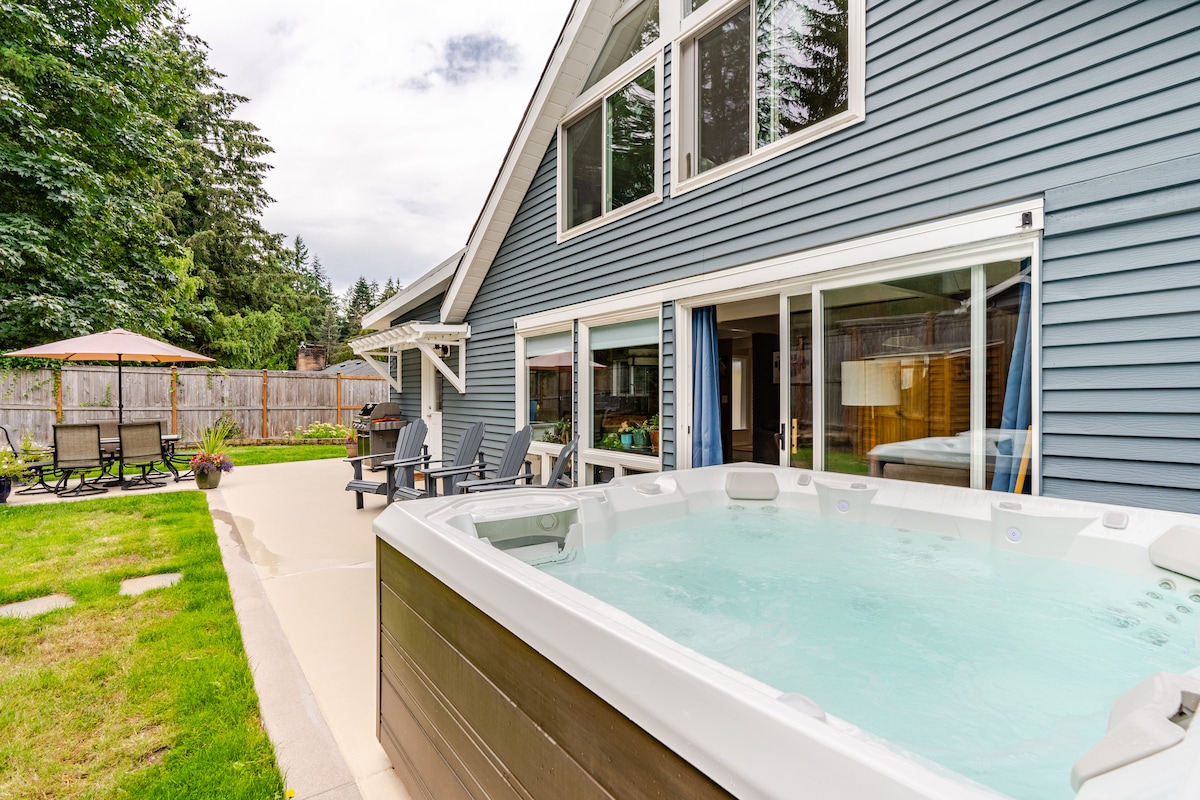A private backyard is highlighted by a saltwater hot tub, surrounded by a spacious patio and landscaped yard. Comfortable outdoor seating is provided with chairs positioned for relaxation. The home features large windows, allowing for ample natural light to fill the space.
