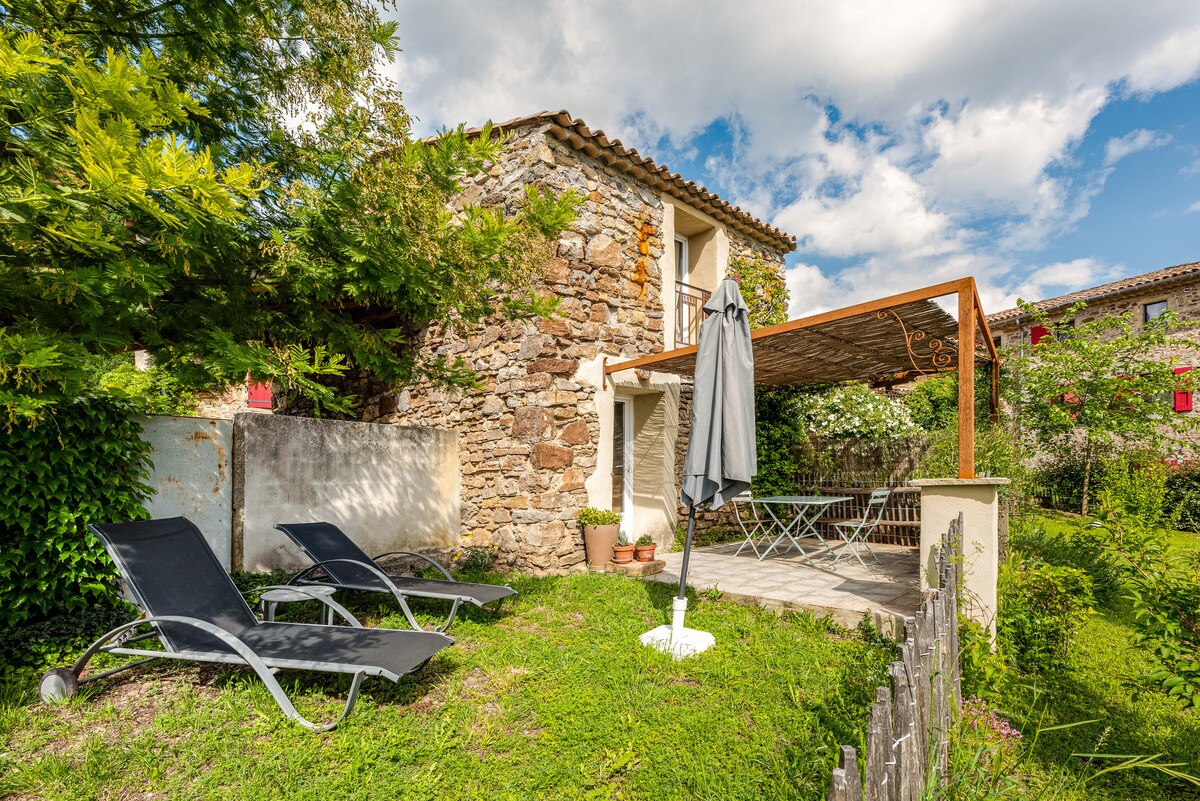 A charming stone building with a wooden pergola is surrounded by lush greenery. Two lounge chairs are positioned on a grassy area, inviting relaxation. The space is adorned with potted plants and features a washing line, enhancing the outdoor living experience.