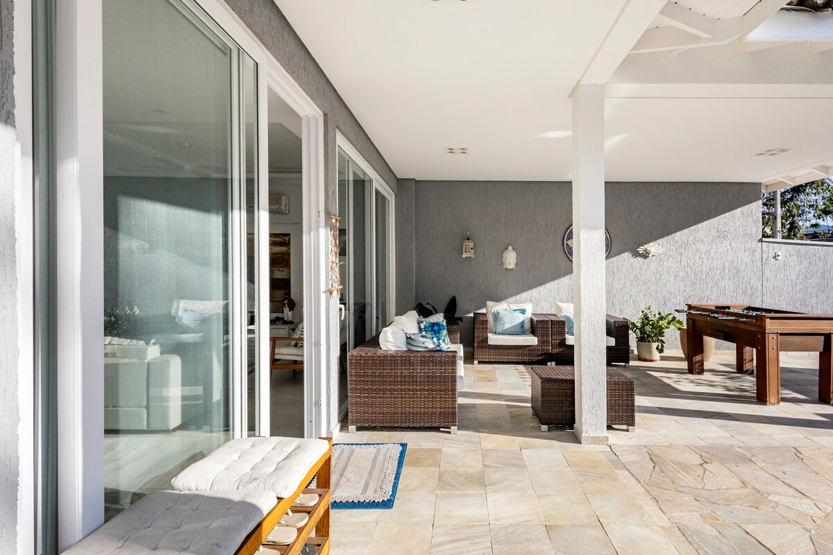 An outdoor seating area is visible, featuring comfortable wicker furniture and decorative cushions. Large sliding glass doors provide access to an interior space, allowing natural light to fill the area. A professional foosball table is positioned towards the right.