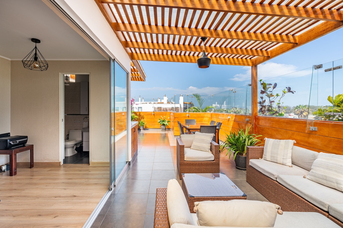 A spacious terrace features a wooden pergola, providing shade over comfortable outdoor seating. The area includes a dining table and potted plants, creating a relaxed atmosphere. Sliding glass doors lead to the interior, enhancing the connection between indoor and outdoor spaces.