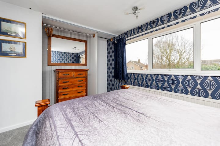 ห้องพักสว่างสดใสพร้อมหน้าต่างบานใหญ่ที่มองเห็นสวนด้านหลังและเตียงขนาดคิงไซส์ ตู้เสื้อผ้าลิ้นชักข้างเตียง