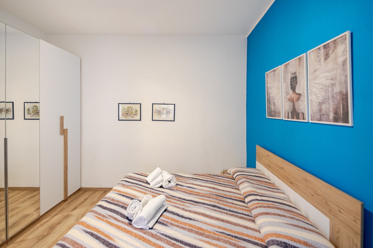 Svetlá a moderná dvojlôžková izba s modrou stenou, veľkou zrkadlovou šatňou a klimatizáciou. Ideálne na oddych v udržiavanom a pohodlnom prostredí po dni strávenom objavovaním krás Viterba.