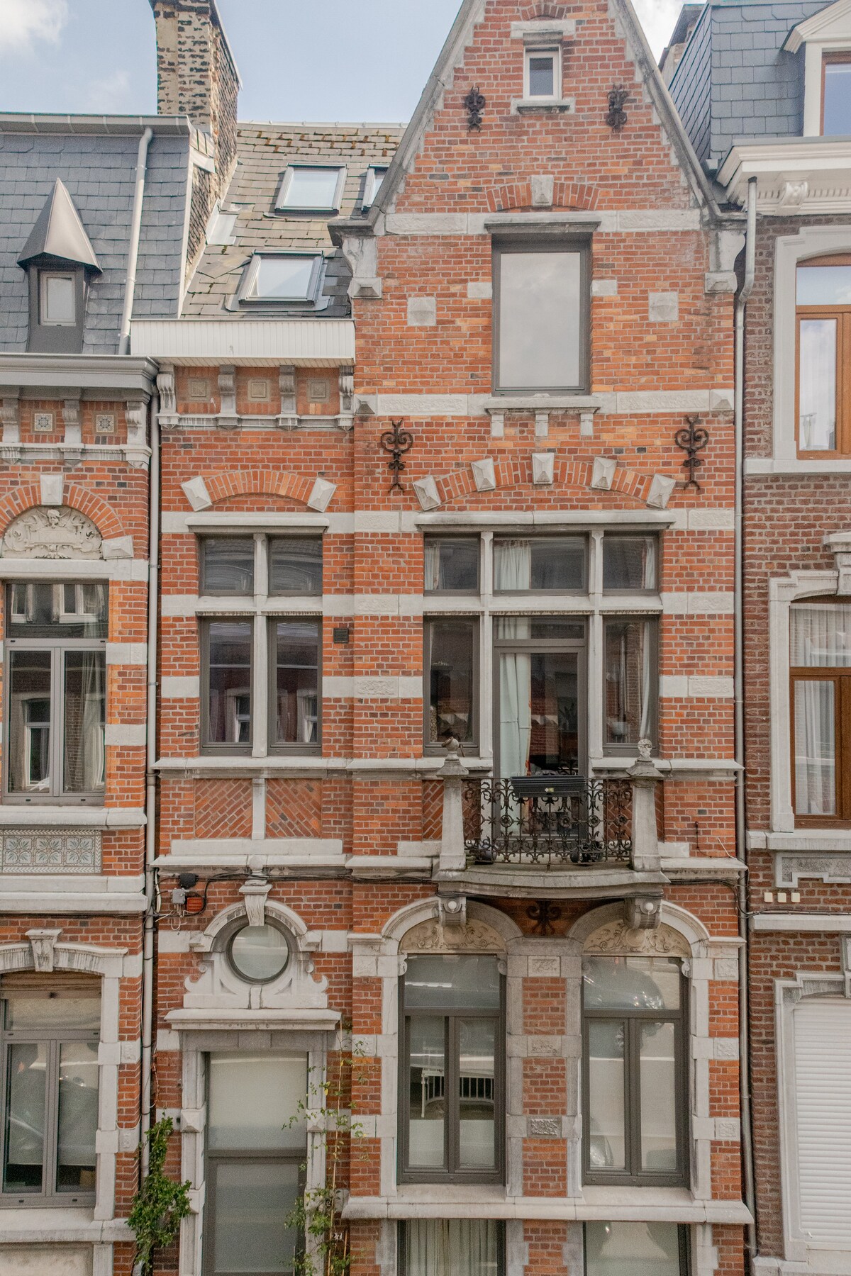 The facade of a historical building is presented, featuring classic red brickwork and intricate stone detailing. Large windows with balconies are visible, allowing natural light to brighten the interior. The architecture reflects a charming, traditional style.