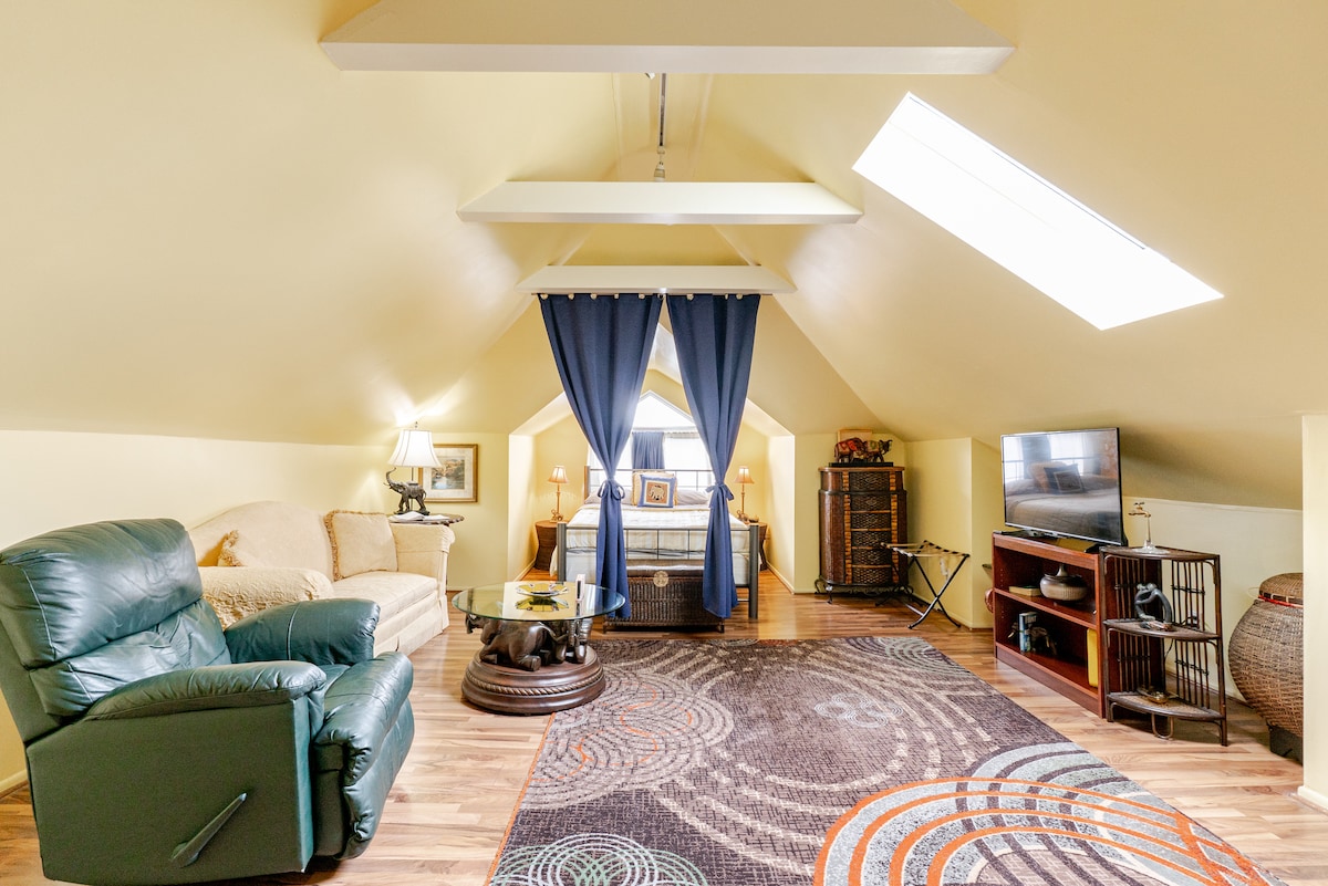 A spacious living area is highlighted by a skylight, providing ample natural light. A comfortable green recliner and a beige sofa are arranged around a round coffee table. Above, decorative curtains create an inviting separation, while a television is positioned on a media console against the wall.